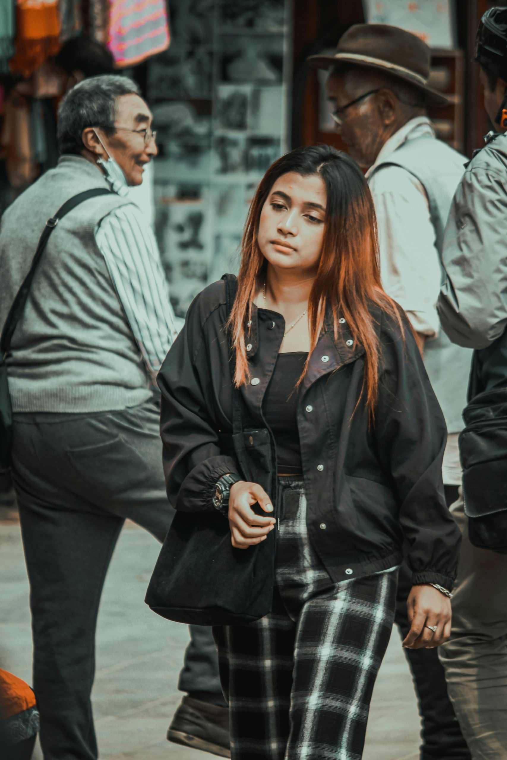A young woman walking through a vibrant street market, lost in thought.